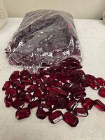 Sealed bag with many red acrylic gems spilling out onto table
