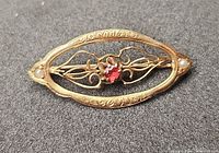 Front of oval gold brooch showing red stone and pearls