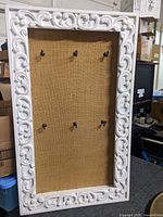 Front view showing ornate frame, burlap panel, six hooks
