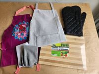 All six items laid out: cutting board, two aprons, oven mitt, pot holder, dish towel