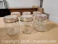 Six clear glass clamp-lid canisters grouped on table