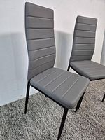 Full view of both gray upholstered high-back dining chairs front angle
