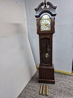 Full view of wooden grandfather clock with three brass weights placed in front