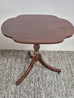 Full view of mahogany pedestal side table showing scalloped top and tripod legs on casters