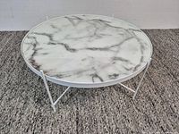 Overall view of round coffee table showing marble-look top and white metal legs