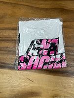 Front of sealed white T-shirt showing pink and black graphic and size label
