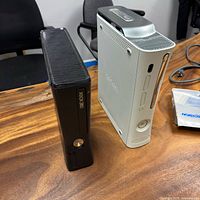 Black and white Xbox 360 consoles with power cable visible