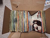 Box containing tightly packed row of 45RPM records in assorted sleeves