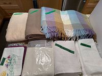 Group view of folded blankets, packaged bedspread, cushion covers, pillowcase and window panels