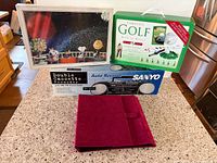 All items grouped on countertop: cassette recorder box, golf set box, sealed Snoopy puzzle, velvet CD binder