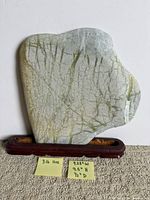 Front of stone slab on display stand (stand not included) showing grey surface with green veining
