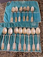 All 14 sterling silver teaspoons on teal cloth rolls