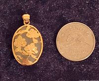 Front of pendant beside 1-cent coin for scale, showing floral overlay and cabochon