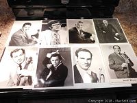 Photo showing the eight autographed black and white photos arranged on a counter, mostly of male celebrities in formal wear, some with musical instruments.