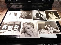 Seven autographed black and white celebrity photos laid out on a black surface including portraits and performance shots