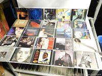 Photo showing a collection of 25 music CDs arranged in 5 rows on a metal rack, showcasing different album covers including Diana Krall, Night and Day, Muddy MacIsaac and more.