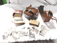 Photo showing three vintage camera cases, Kodak film box, two smaller boxes, and multiple black and white photographs spread out in front.