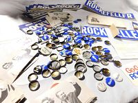 Wide shot showing collection of campaign buttons, postcards, and bumper stickers scattered on surface.