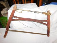 Side view of antique wooden and metal frame saw with horizontal metal blade and wooden tensioning handle.