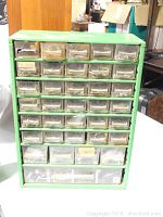 Front view of green hardware storage chest showing all small transparent drawers and some metal fasteners inside.