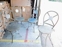 Four dusty and worn metal chairs with circular backs and curved legs grouped together near boxes.