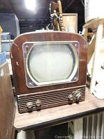 Front view of antique TV set showing rounded CRT screen, three control knobs, and wooden cabinet with visible wear.
