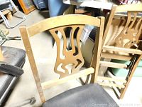 One vintage wooden folding chair with black padded seat from the back, showing detailed cut-out design.