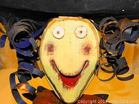 Close-up of witch face showing painted features and black curled metal hair.