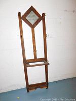 Front view of the antique wooden hall tree showing diamond-shaped mirror and metal hooks