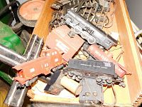 Photo of multiple train cars including a red caboose, black boxcar, and various track pieces in a wooden box.