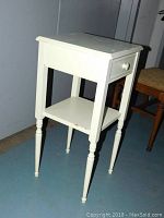 Front left angle view of the light mint green shabby chic side table showing top, drawer, shelf and turned legs.