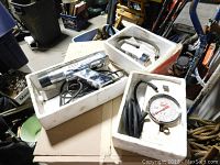 Overview of the 3 auto repair tools in white styrofoam boxes placed on a surface inside a garage with various items around