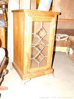 Side angle view of wooden cabinet showing detailed glass front with diamond-shaped leads and silver decorative feet