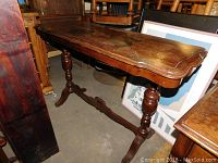 Side angled view of antique wooden hall table with shaped top and turned legs, showing wear and one leg detached from base.