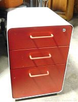 Front view of white and red filing cabinet with three closed drawers and lock on top drawer.