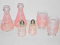 Photo showing two pink and clear glass beakers, two glass salt and pepper shakers with metal lids, and two pink textured glass tumblers arranged on a white background.
