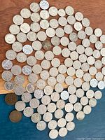 Wide view showing the full assortment of approximately 100 small Canadian nickel coins laid out on wood surface