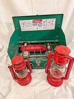 Open Coleman 425E stove with two red hurricane lanterns in front