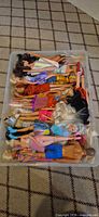 Plastic bin containing roughly twenty dressed Barbie and Ken dolls