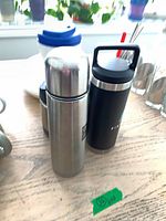 Stainless vacuum flask, black insulated bottle, other drinkware items visible