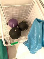 Three medicine balls and a deflated blue balance ball inside a white wire basket