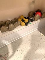 Shelf section holding multiple gold rubber-coated dumbbells, yellow and black vinyl dumbbells