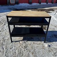 Front view of workbench showing plywood top, two shelves, black metal frame