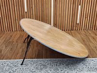 Round plywood table angled on floor showing top surface and missing leg