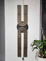 Full view of tall Bauhaus wall sculpture mounted on white wall beside plant