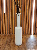 Full view of tall white art glass floor vase on wooden floor
