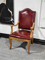 Front view of red leather armchair showing upholstery, nailhead trim, carved wood arms and legs