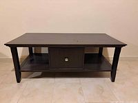 Front view of rectangular dark wood coffee table showing top, legs, lower shelf, and center storage door