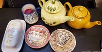 All items laid out: butter dish, coffee mug, two teacup/saucer sets, two teapots