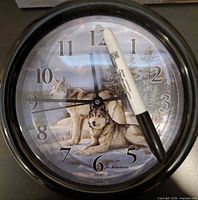 Front view of wall clock showing wolf artwork, numerals, hands, black frame